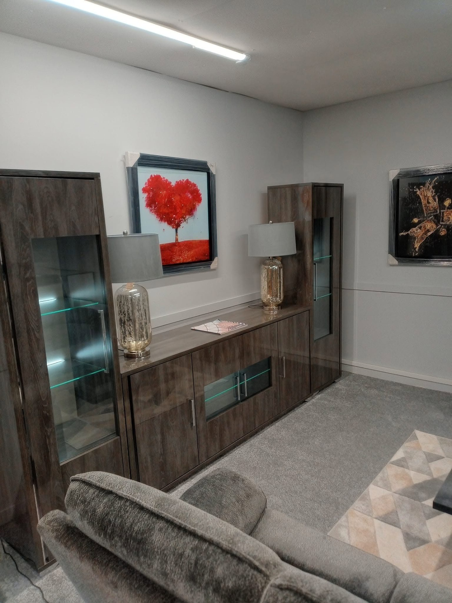 Dark wood lounge display cabinet with lit glass shelves, part of a furnished living room
