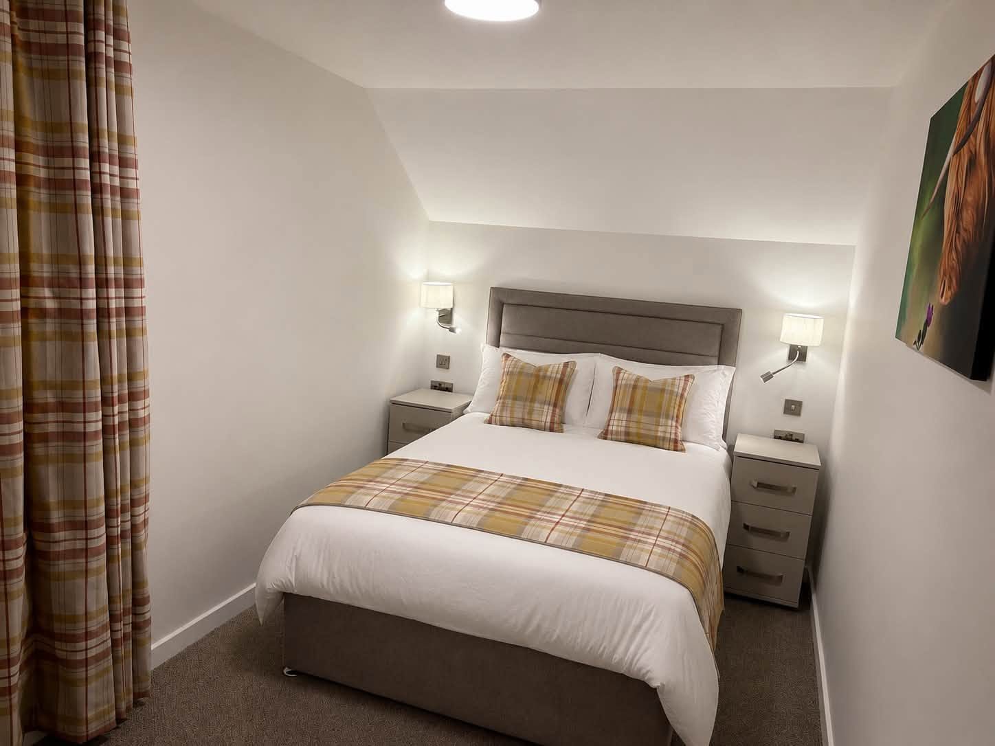 Furnished bedroom with grey upholstered headboard and mustard tartan runner and cushions