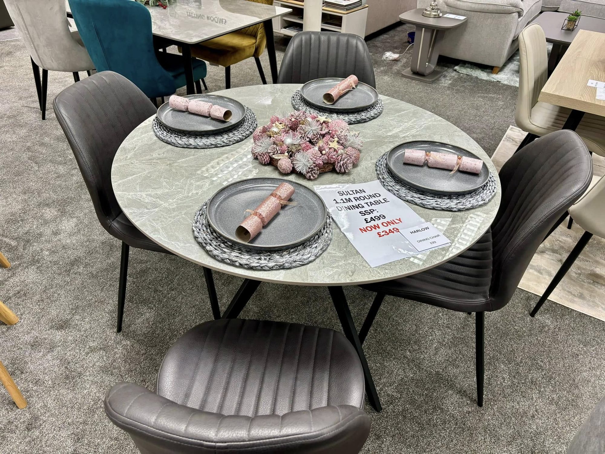 Round marble-top dining table with four grey upholstered chairs on the showroom floor