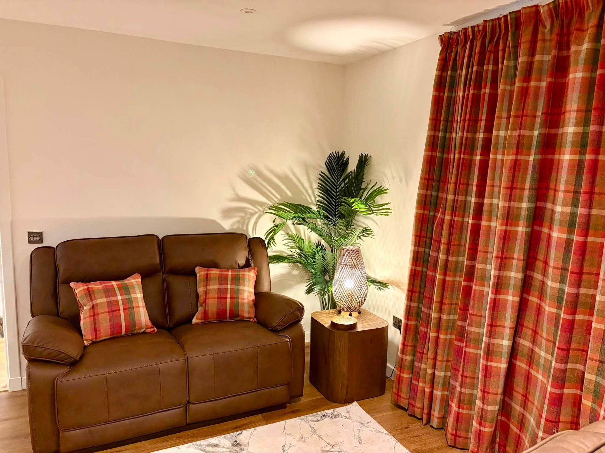 Red and green tartan curtains beside a brown leather sofa with tartan cushions