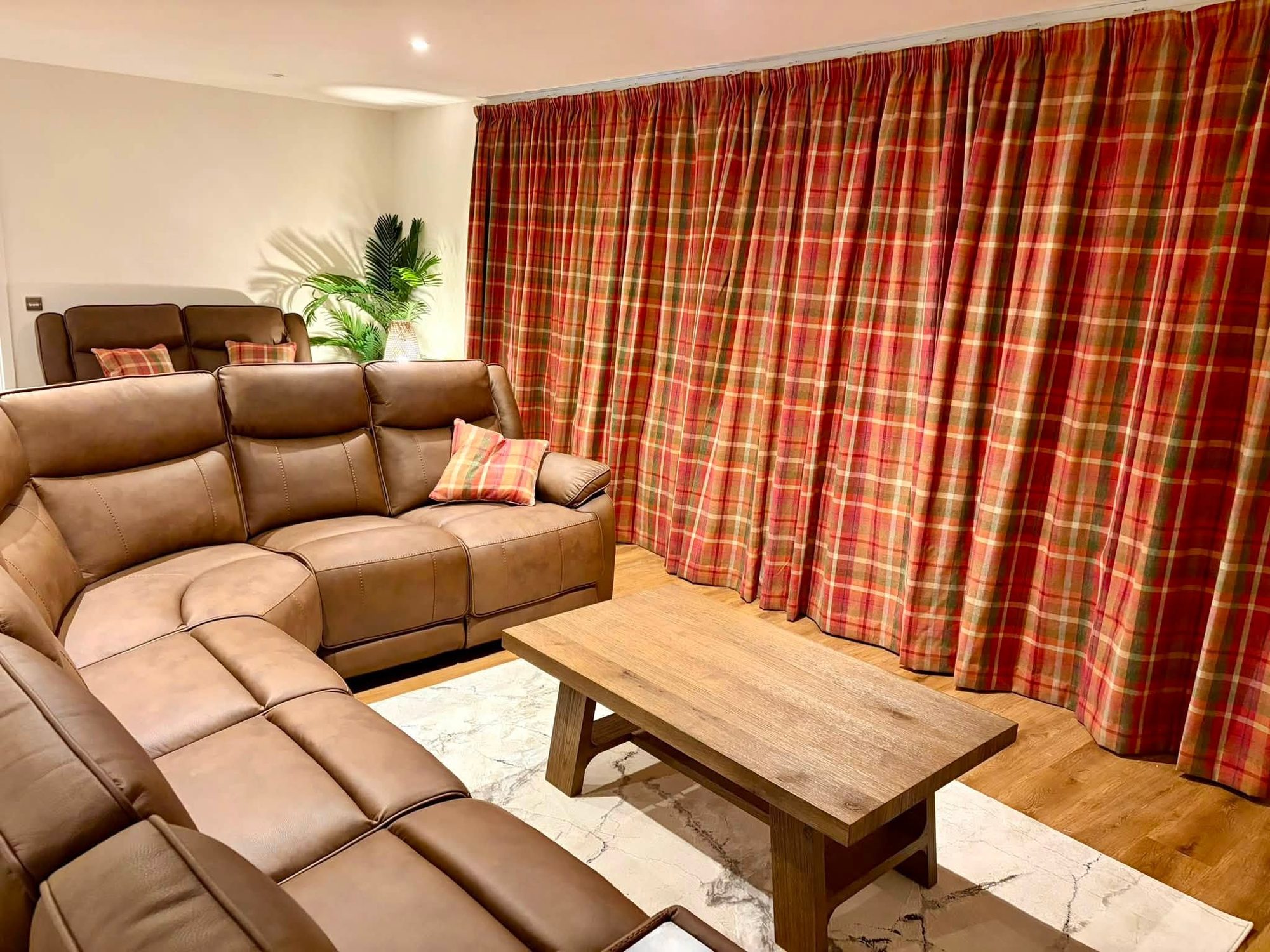 Full-width tartan curtains dressing a living room window behind a leather corner sofa