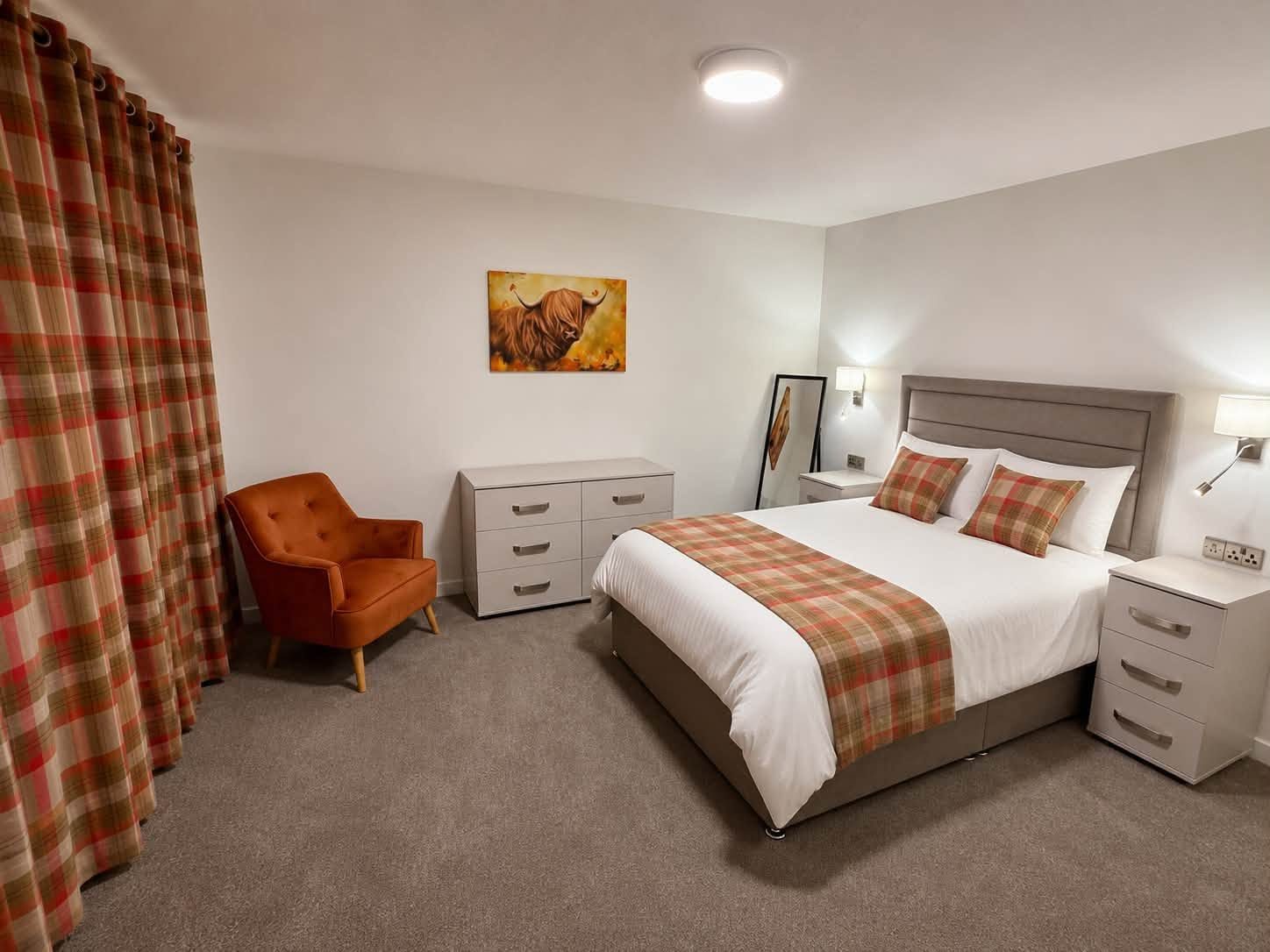 Furnished bedroom with grey bed, tartan accents and an orange upholstered armchair