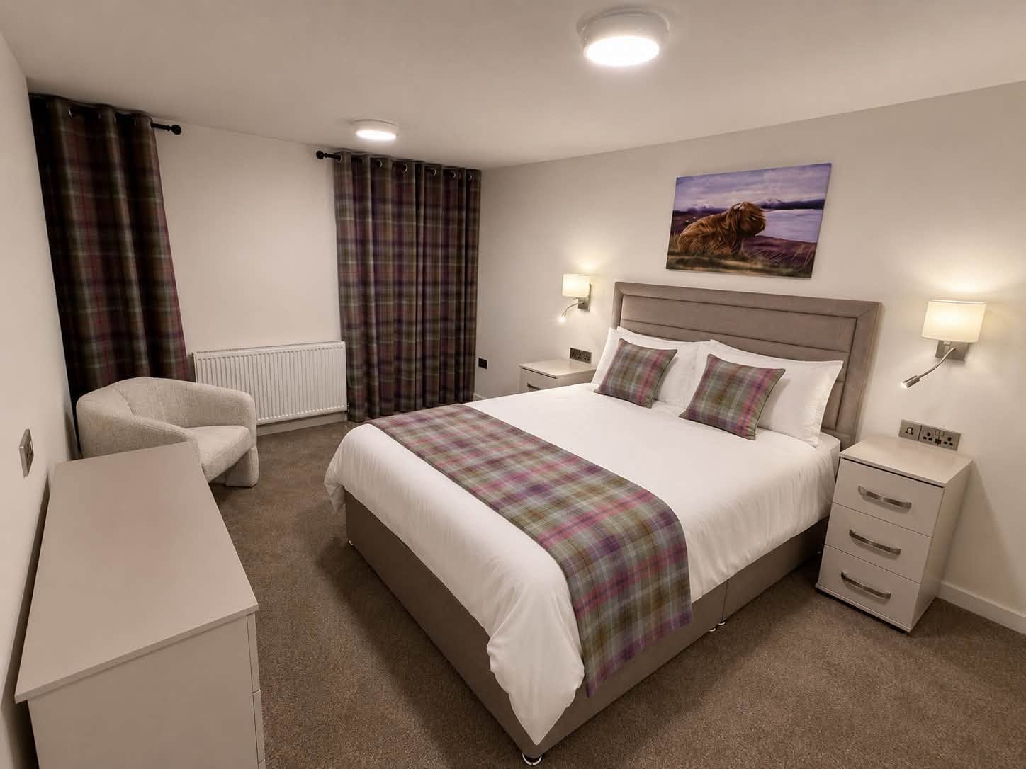 Furnished bedroom with purple tartan runner, cushions and a textured white armchair