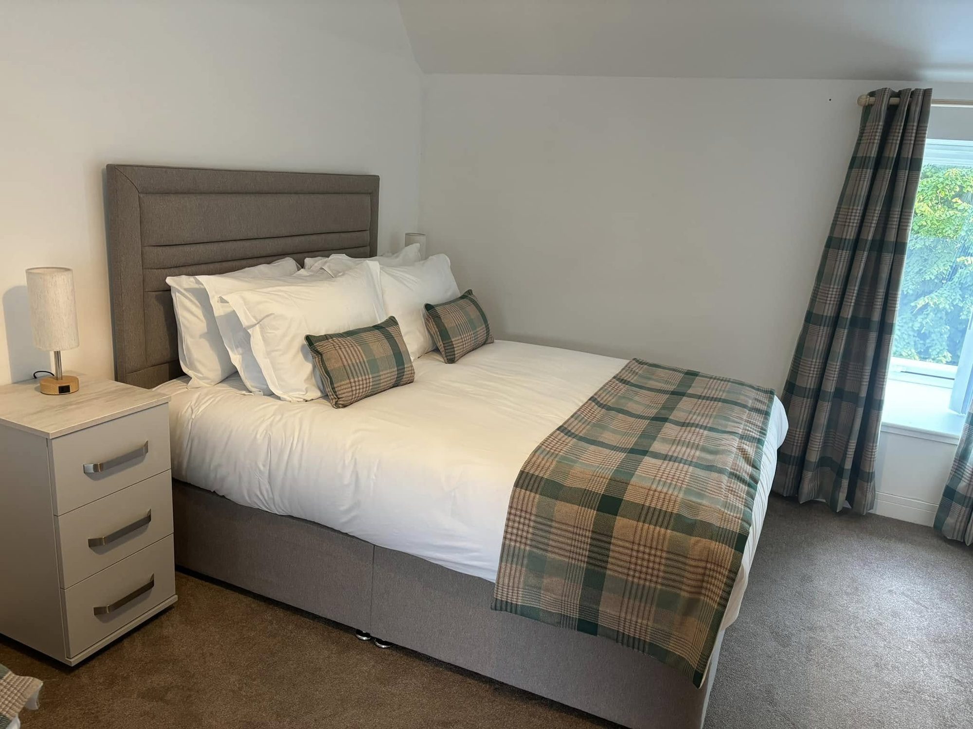 Double bed with grey headboard and green and red tartan cushions in a furnished bedroom