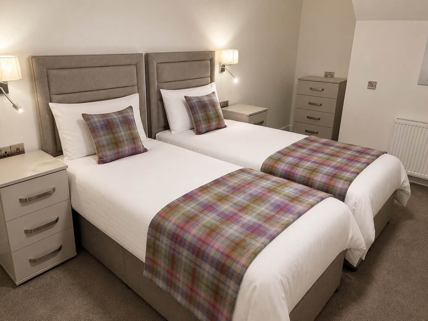 Twin beds with grey upholstered headboards and tartan runners, furnished by Taylor's of Keith