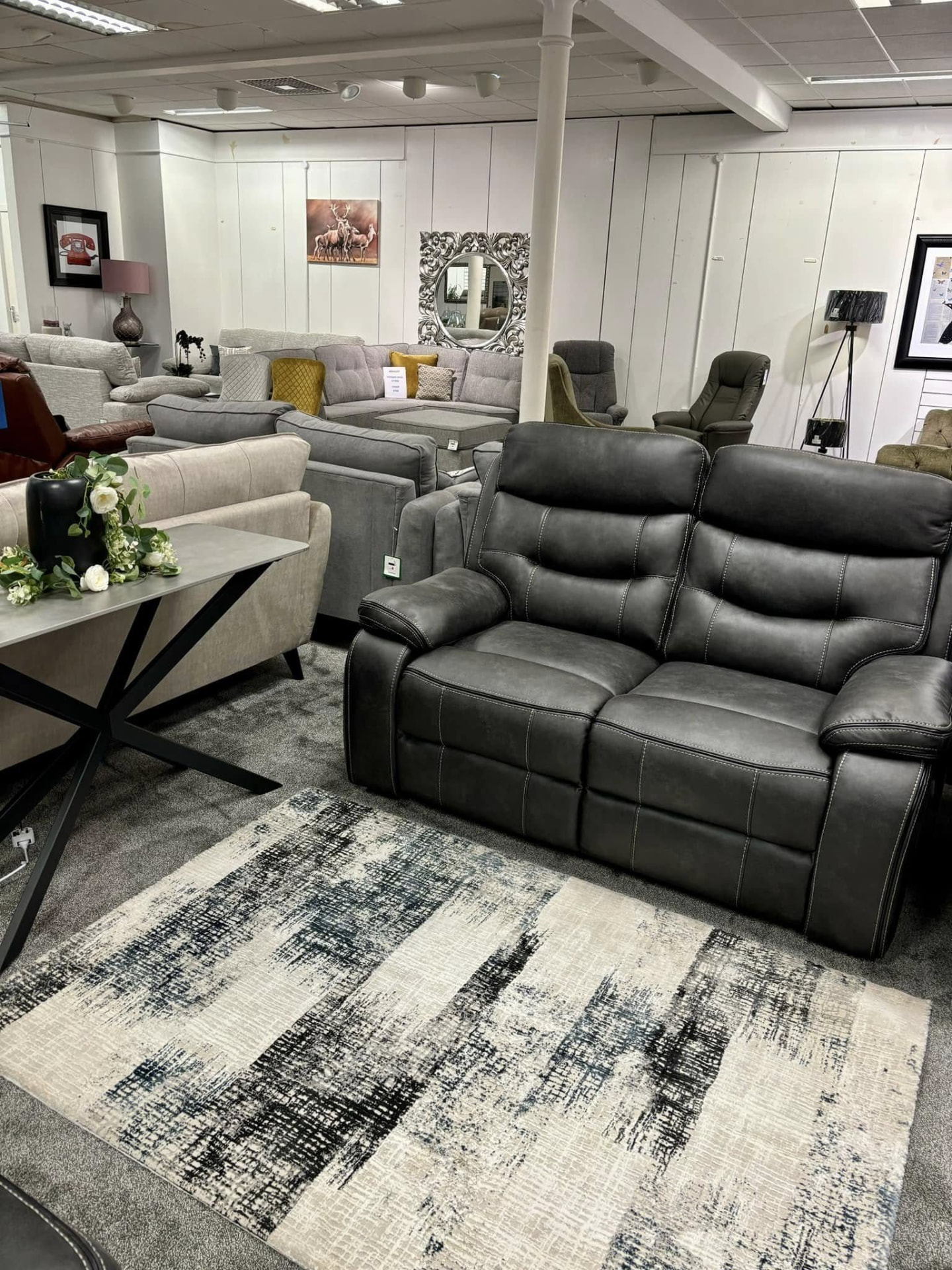 Dark grey recliner sofa in the Buckie showroom beneath Highland deer artwork